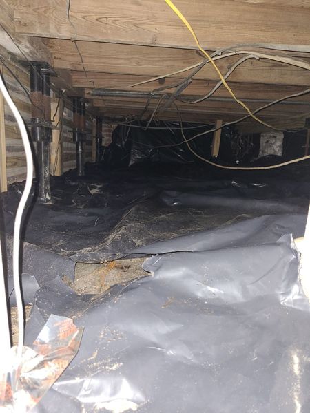 Crawl space with vapor barrier installation showing plumbing and structural supports