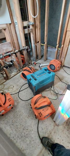 Residential water damage drying setup with blue dehumidifier and orange air movers in flood-cut room